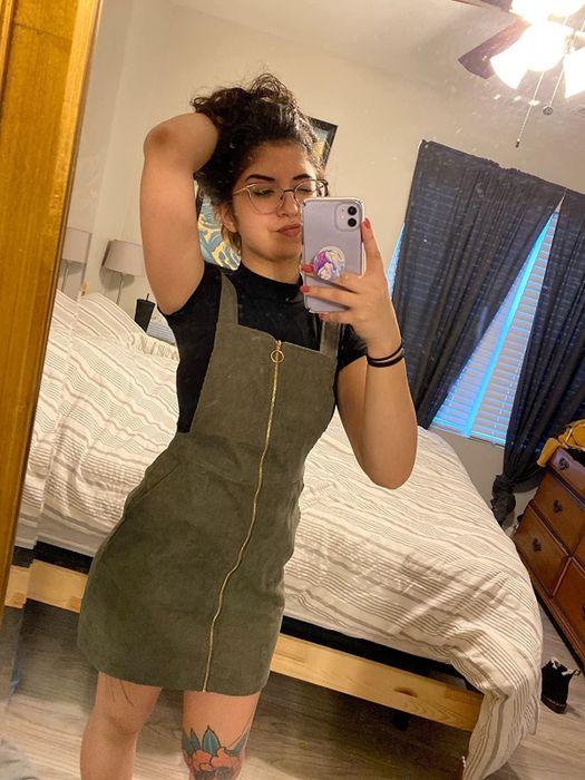 A reviewer posing in front of a mirror, wearing a green pinafore dress