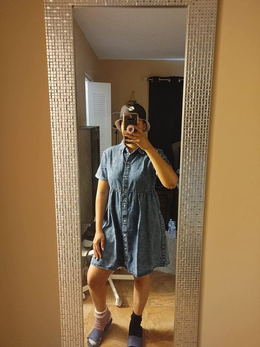 A reviewer posing in front of a mirror while wearing a blue denim mini dress