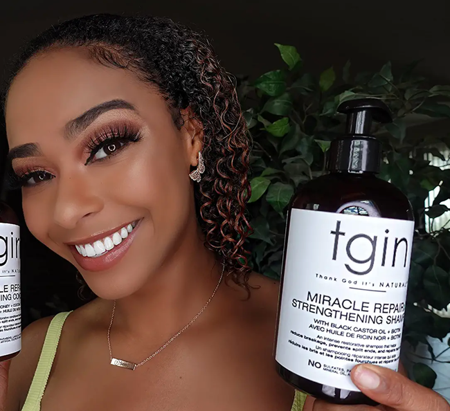 Model holding a black pump bottle of shampoo in front of a plant.