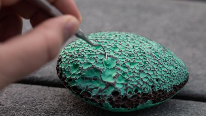 A model using a small hook to extract blue paint from a porous lava rock