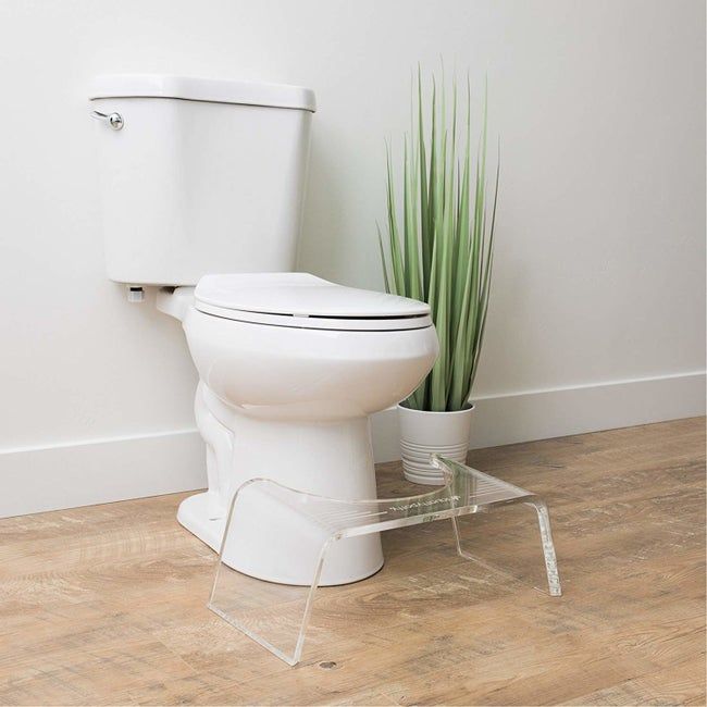 A clear step stool with a rounded side placed next to a toilet.