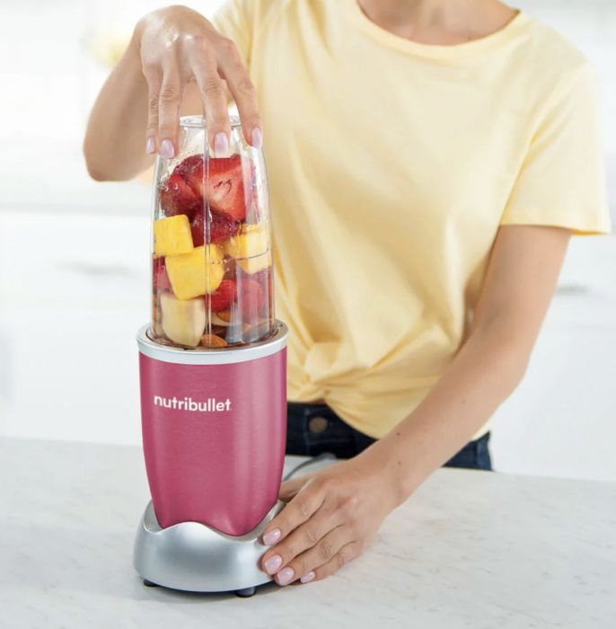 A person blending fresh fruit in the vibrant pink Nutribullet blender.