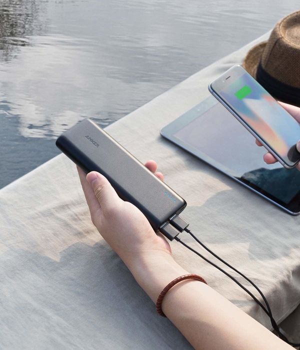 A hand gripping the slim, rectangular charger with a cord plugged into a phone, indicating it's charging.
