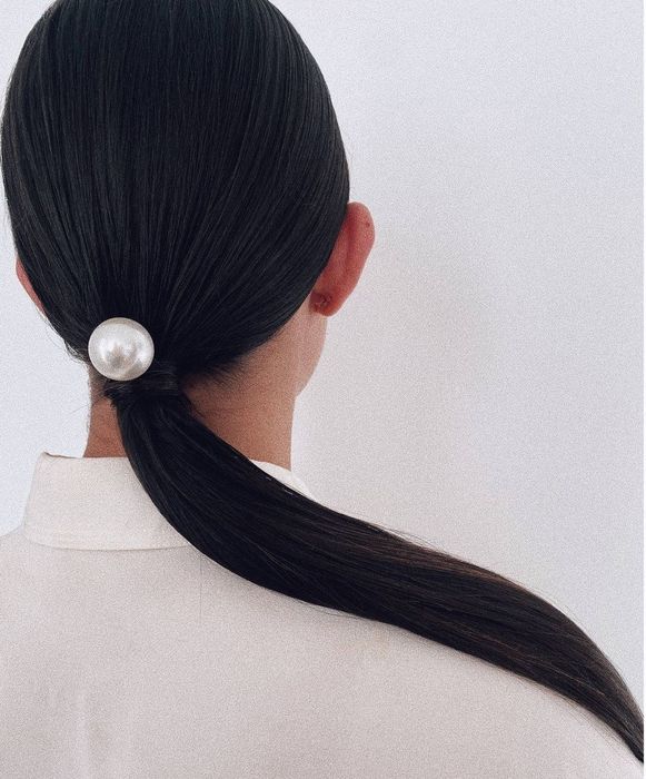 Model with black hair in a ponytail, wearing a pearl clip