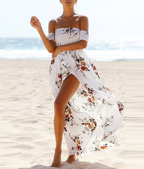 A model dressed in a flowing, long off-shoulder white dress adorned with a floral pattern.