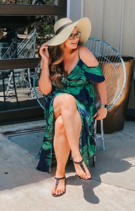 A reviewer seated in a green leaf print maxi dress, complete with a floppy hat.