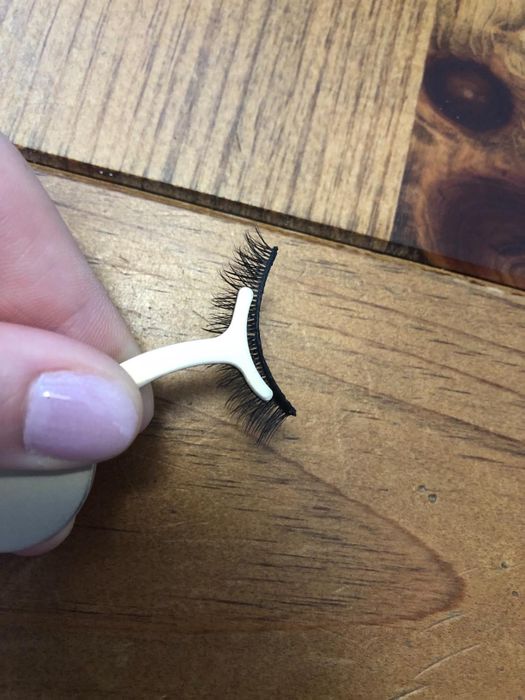A hand holds a pair of false eyelashes along with a small applicator tool.