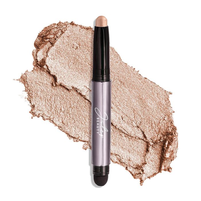 A Julep beauty eyeshadow stick featuring a dual-ended design with a crayon tip for smooth application and a smudger for seamless blending rests on a textured backdrop of shimmering eyeshadow.