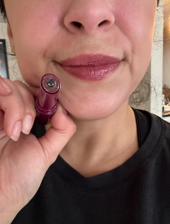 A person applying lipstick, showcasing a soft, glossy makeup style