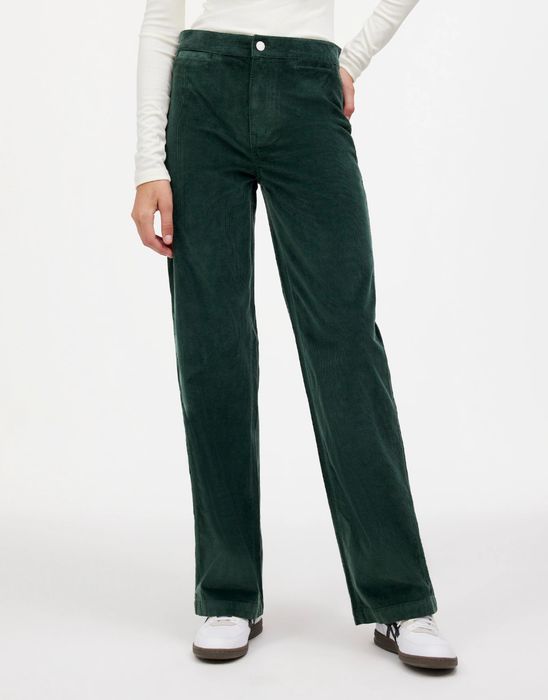 A person is sporting high-waisted corduroy pants and sneakers, standing against a simple white background
