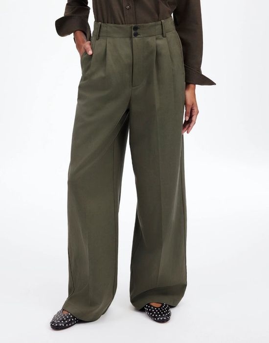 Person wearing wide-leg trousers, hands casually tucked in pockets, paired with polka dot shoes and rolled-up shirt sleeves. A stylish and laid-back outfit.