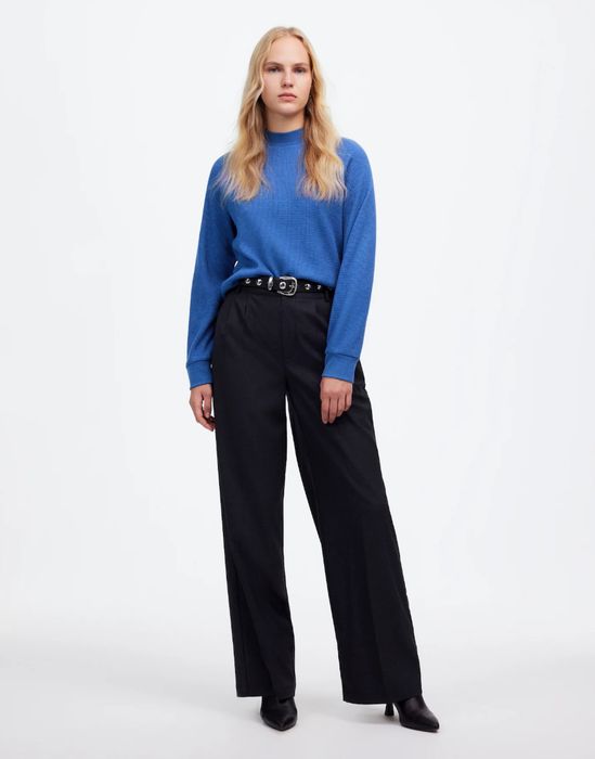 Person wearing a blue sweater, black wide-leg pants, and black heels, posed against a simple background.