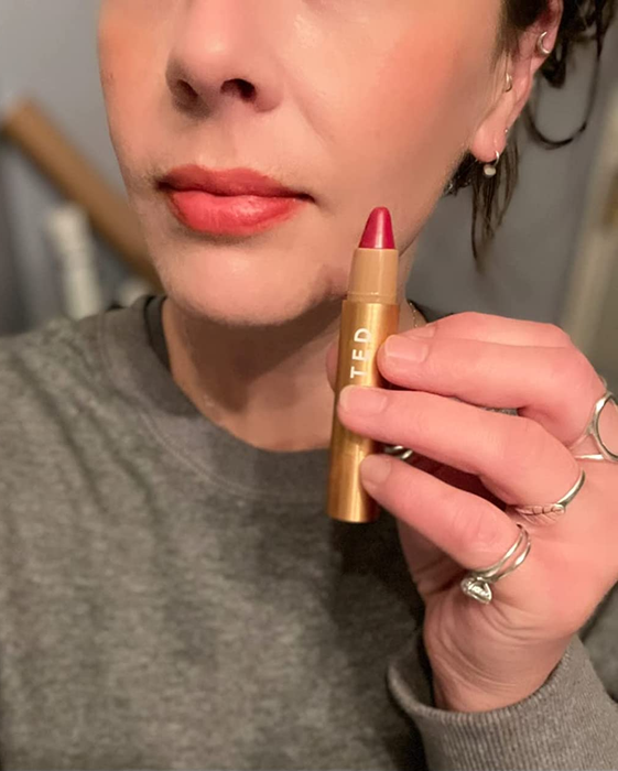 A reviewer holding the Huestick next to their lips, which are adorned with a reddish-orange hue.