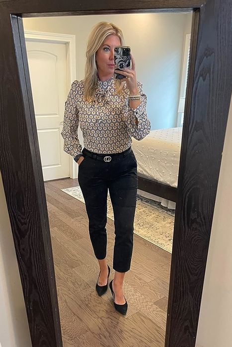 A reviewer showcasing a mirror selfie, dressed in black slacks paired with a blouse and heels.