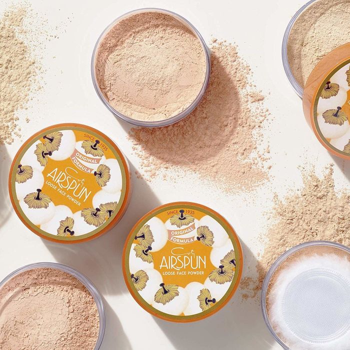 Tubs of Coty Airspun face powder with a scattering of powder in the background, capturing its silky texture.