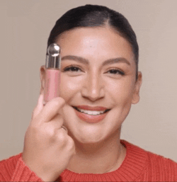 A gif of a model applying two dots of blush to each cheek, blending it out with a brush and their finger.