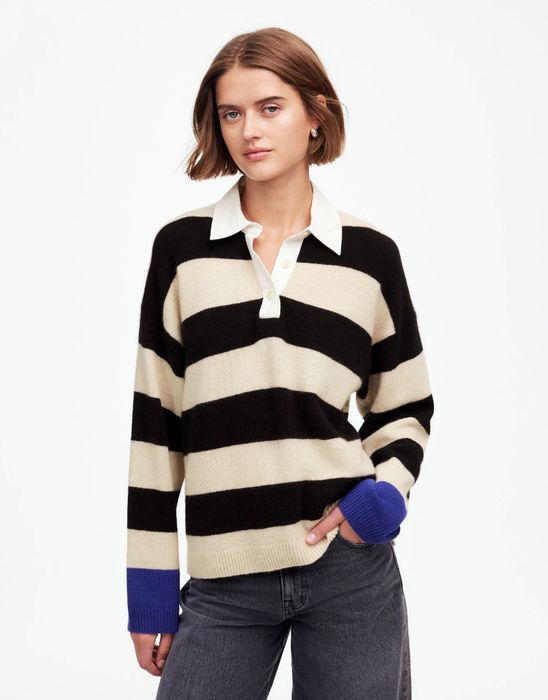 A person is seen wearing a striped sweater with a collar and jeans, standing with a neutral expression against a plain backdrop