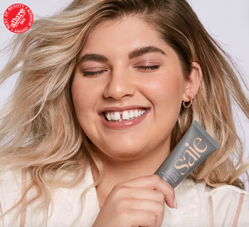 model wearing the tinted moisturizer while holding the product in shade Three: Light to Medium Peach