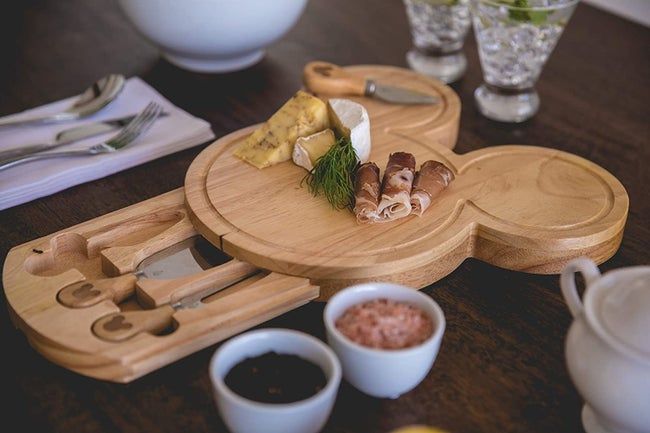 a wooden Mickey-shaped cheese board with a drawer filled with cheese knives