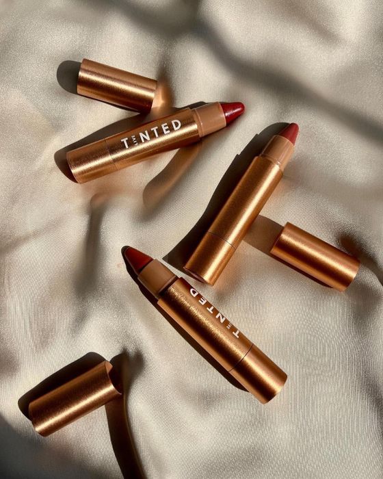 Lip crayons are spread out on a fabric surface, their caps removed to highlight their elegant and streamlined design.
