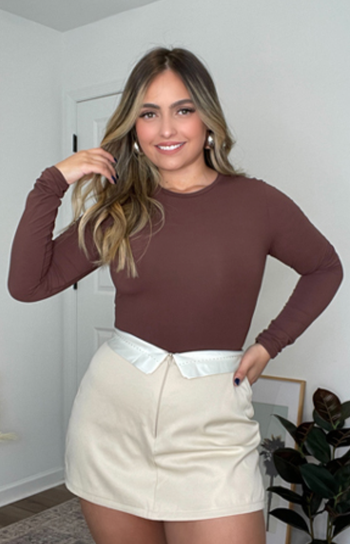 A model wearing the brown version of the bodysuit tucked into a mini skirt
