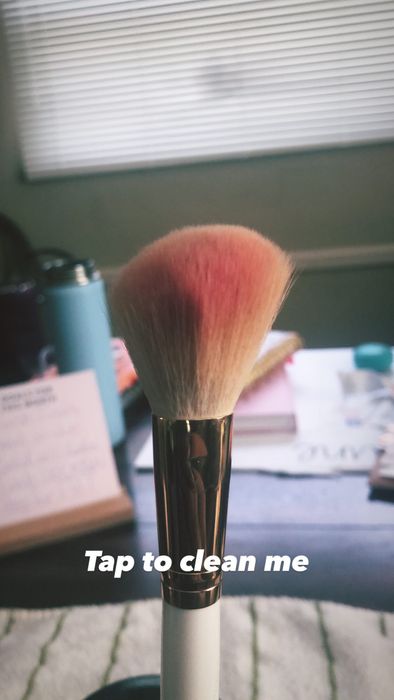 A makeup brush with red blush residue on the bristles.