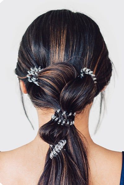 A model displays three clear hair ties in their hair.
