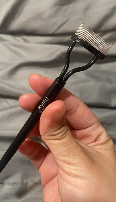A reviewer holding the black eyelash separator comb in their hand
