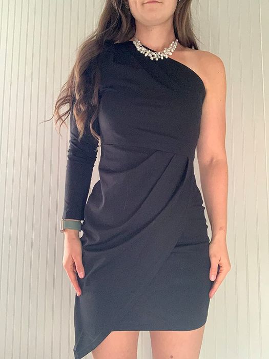 A close-up of a reviewer wearing the black version of the product, accessorized with a pearl chunky necklace, set against a white wall.