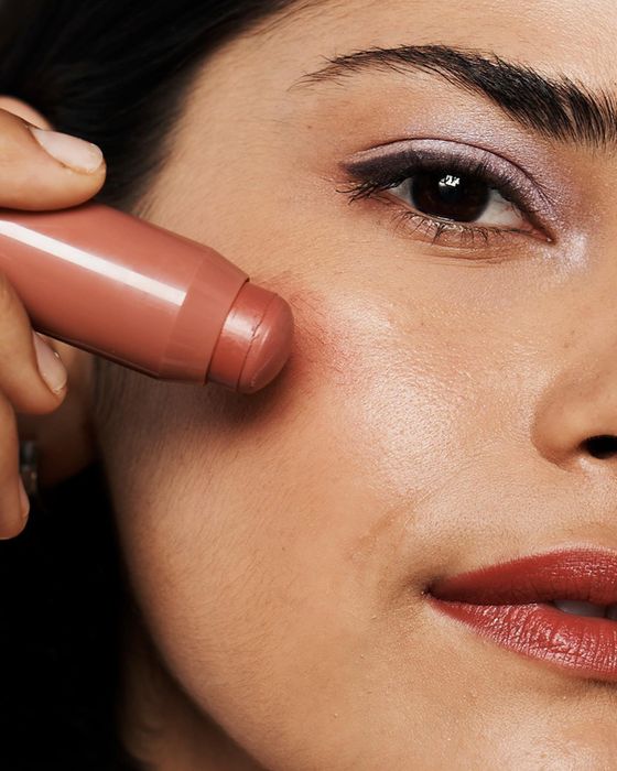 A model applying a rosy-hued color balm to their cheek.