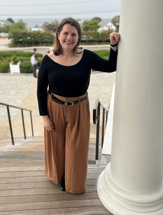 A person rocking a chic off-the-shoulder top and wide-legged pants while standing on outdoor stairs next to a pillar.