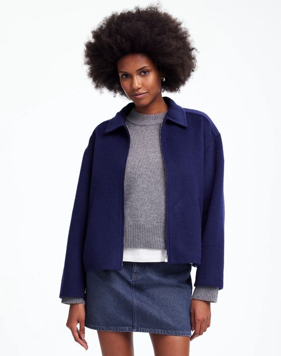 A person showcasing a laid-back look, wearing a dark jacket over a gray sweater paired with a denim skirt, perfect for a casual shopping day.