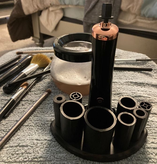 A reviewer's brush cleaner with a stand and cleaned brushes in the background next to a bowl filled with dirty water.