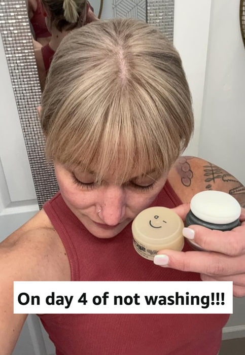 A model with bangs holding hair products, visible in a mirror reflection; accompanying text reads
