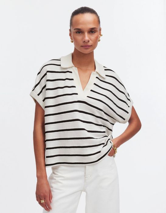 Person confidently posing in a striped short-sleeve polo shirt paired with white pants, gazing directly at the camera.