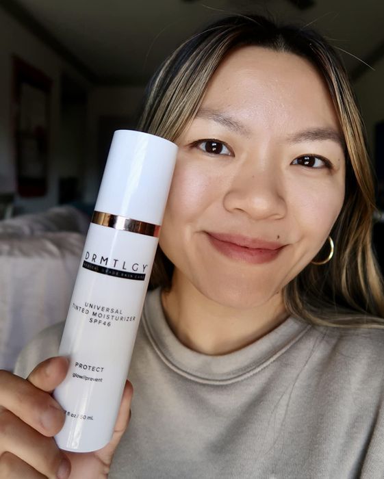 selfie of a reviewer showcasing the tinted moisturizer while holding the product bottle