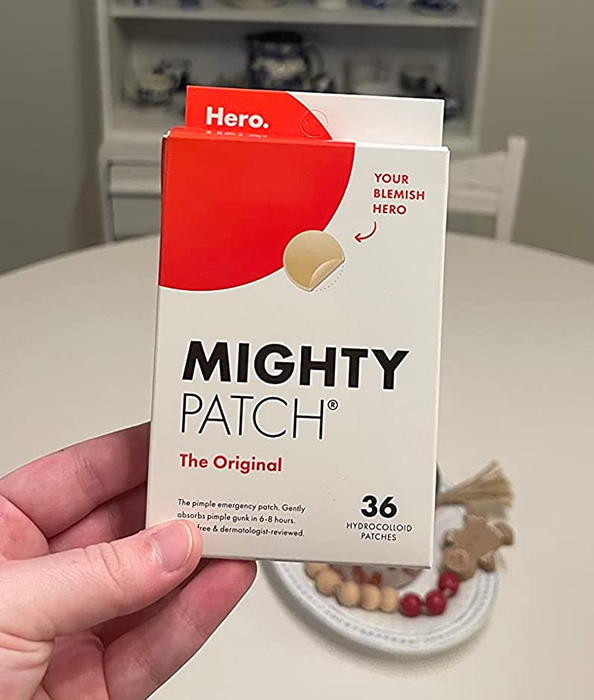 The reviewer holding a box of Mighty Patch, with white and red packaging.