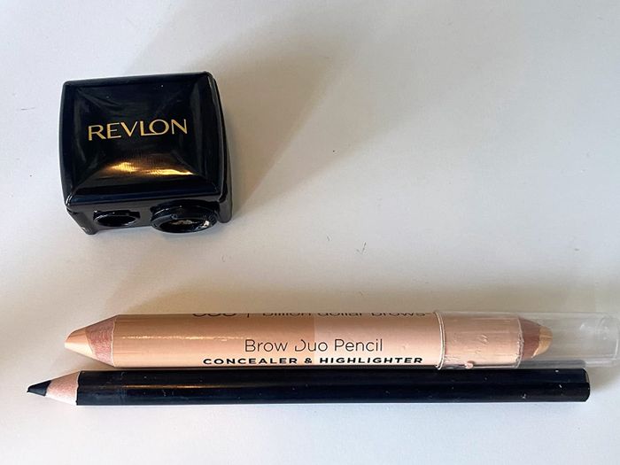 A Revlon Dual Sharpener showcasing a thin eyeliner pencil and a jumbo concealer pencil, both sharpened to perfection.