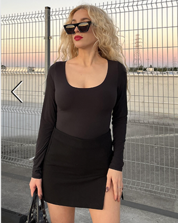 A model wearing a black long-sleeved bodysuit tucked into a mini skirt