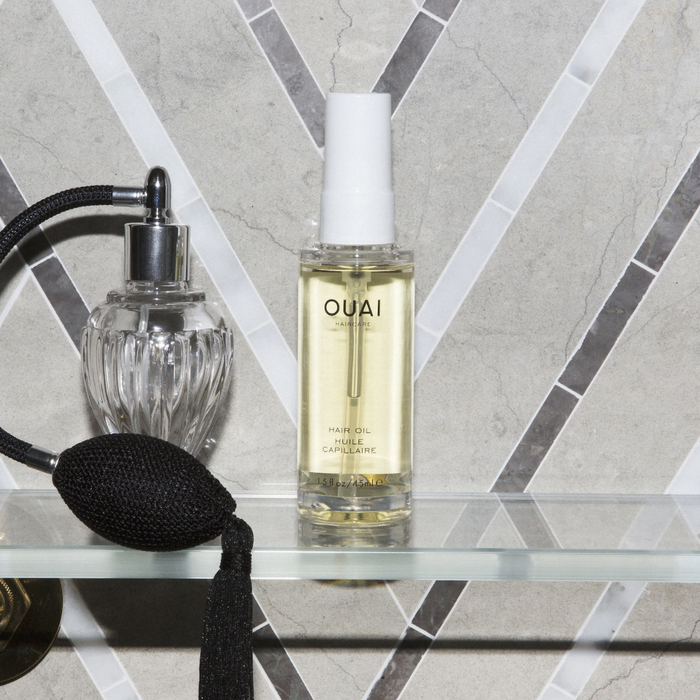 The bottle of Ouai Hair Oil placed next to a perfume bottle on a chic countertop