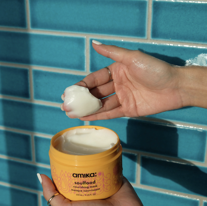 Hand scoops out Amika Soulfood Nourishing Mask from its orange jar