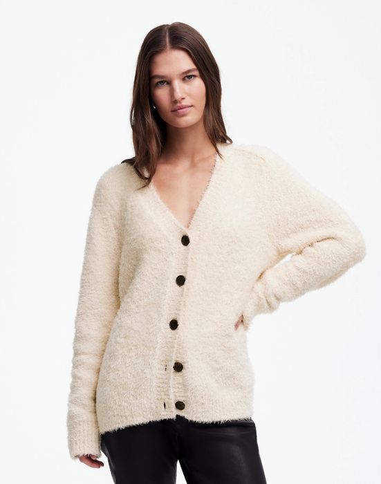 A person sporting a soft, button-up cardigan paired with sleek leather pants, posing against a simple background.