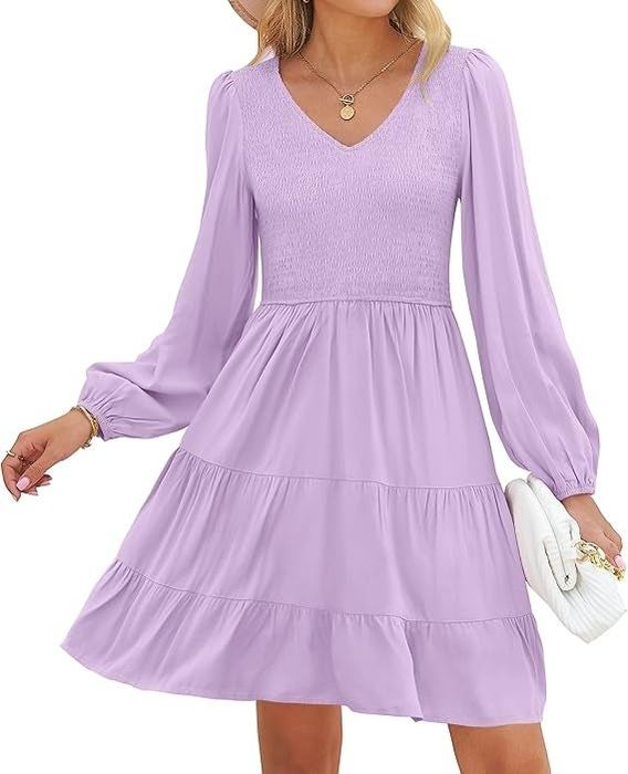 A model wearing a flowing, V-neck dress with long sleeves, holding a white clutch.