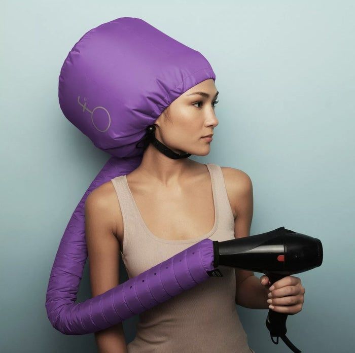 A woman wearing a hair dryer hood while holding a blow dryer