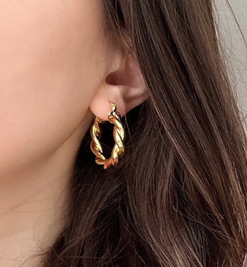 A close-up of a person wearing a bold, chunky gold hoop earring, highlighting its statement-making appeal.