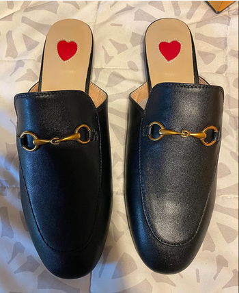 Black leather loafers featuring gold horsebit accents and red heart-shaped insoles