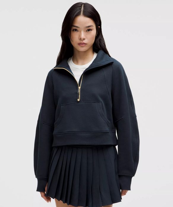 A model wears a chic zip-up sweatshirt paired with a pleated skirt, standing against a neutral backdrop.