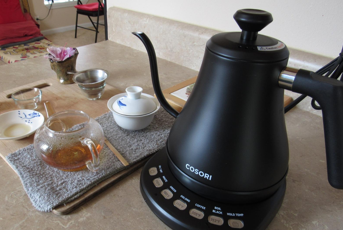 A reviewer displays the sleek black kettle alongside a cup of tea brewed with it.