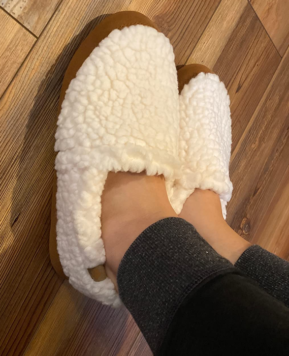 A close-up of a reviewer wearing the white slippers, showing off the fluffy comfort
