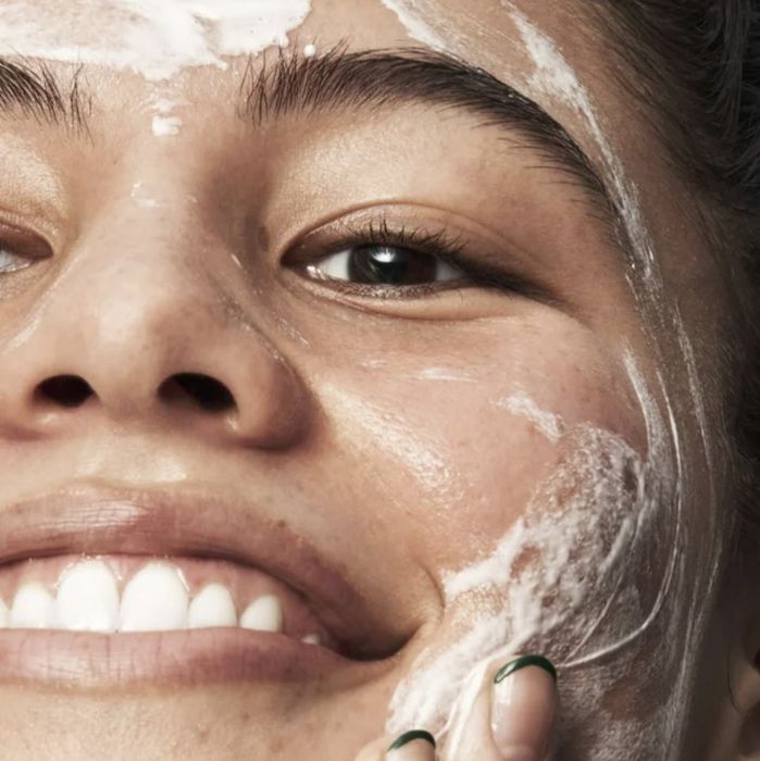 A close-up of a person smiling with facial cleanser applied to their face